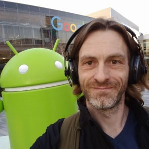 The same photo of Dirk Primbs beside the green Android statue, cropped square, with a Google building sign behind.